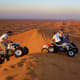 Two riders on ATVs on golden sand dunes in desert landscape at dusk, Jeddah